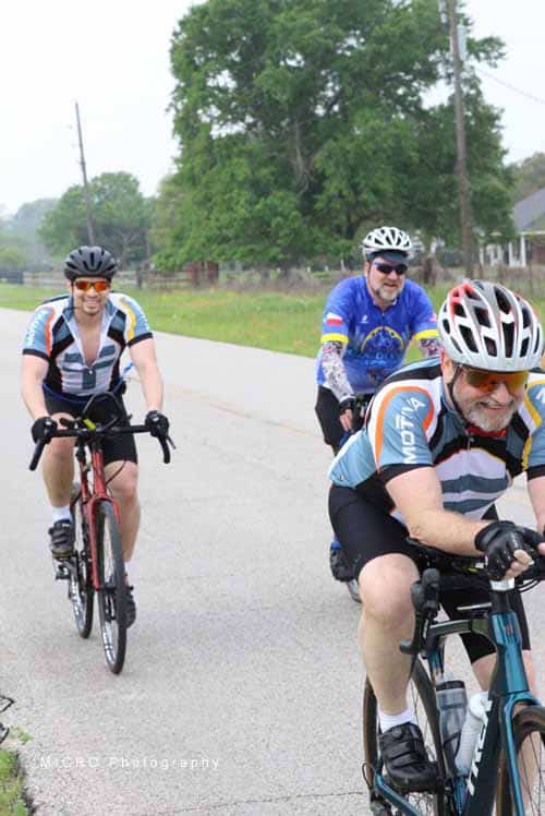 Vibrant group of cyclists riding on a scenic road with greenery and trees in the background, promoting outdoor biking fun.