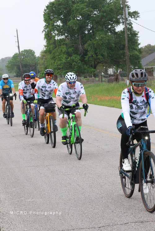 Group of cyclists riding on a rural road during day, promoting Bluebonnet Express bike event.