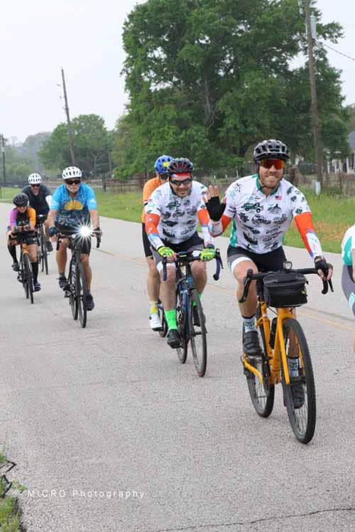 Cyclists enjoying Bluebonnet Express event on a scenic rural road with lush greenery and community spirit.