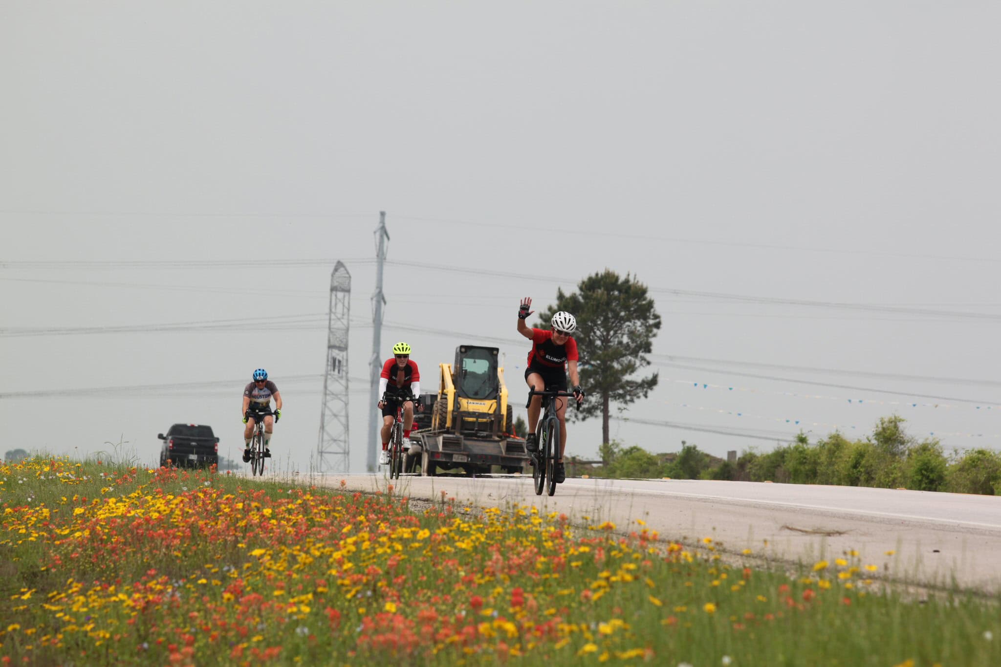 Bright bluebonnet express cyclists riding on scenic highway with construction vehicle in background.