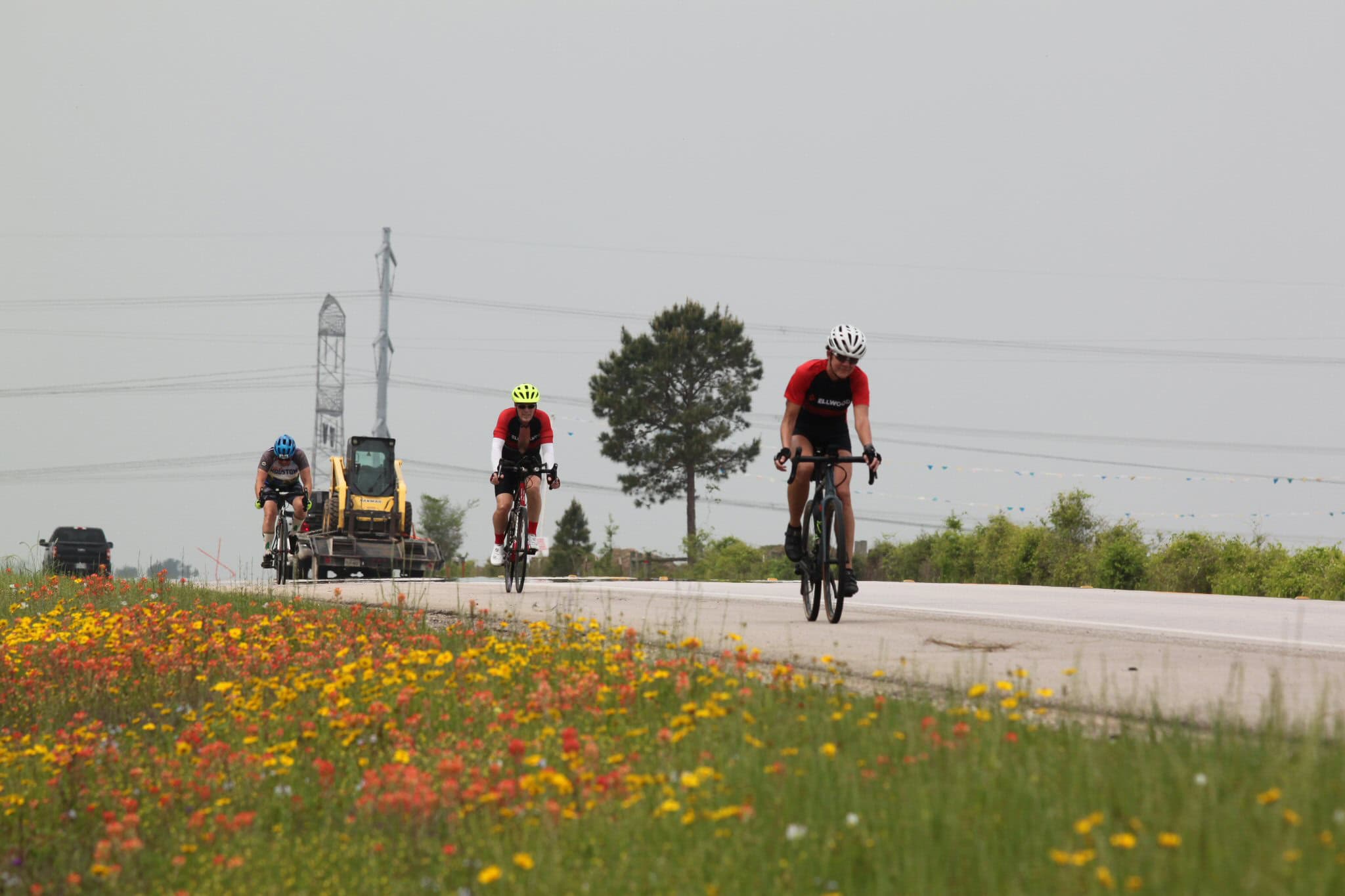 Cyclists riding on a rural road with construction equipment in the background, promoting eco-friendly transportation.