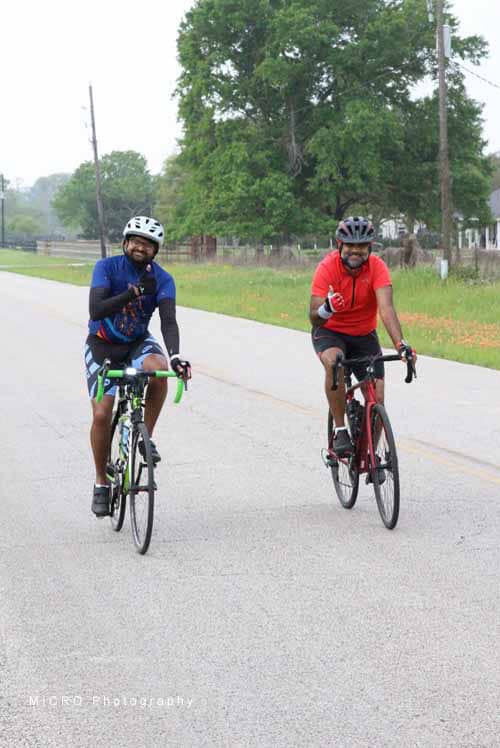 1. Two cyclists enjoying a ride on a rural road with lush green trees in the background.