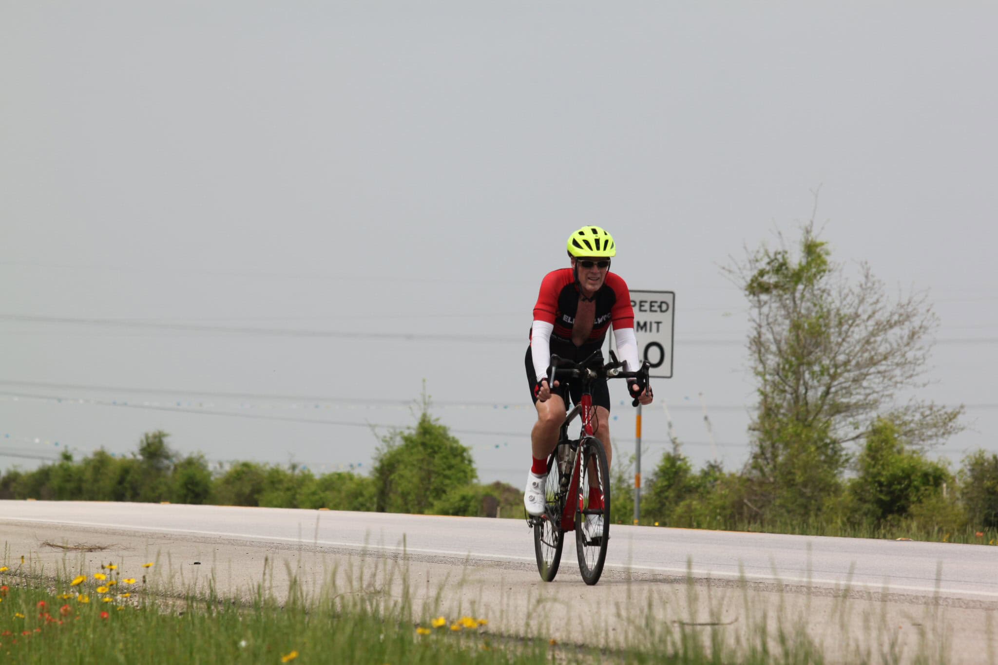 Bright cyclist in red and black riding on open road with greenery and speed limit sign behind, promoting outdoor biking adventures.