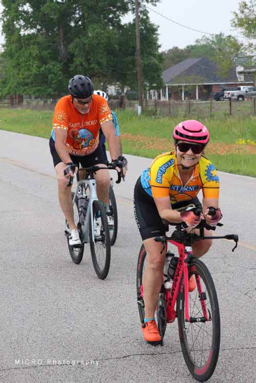 Bright female cyclist wearing a pink helmet and orange Jersey on a scenic Bluebonnet Express bike route.