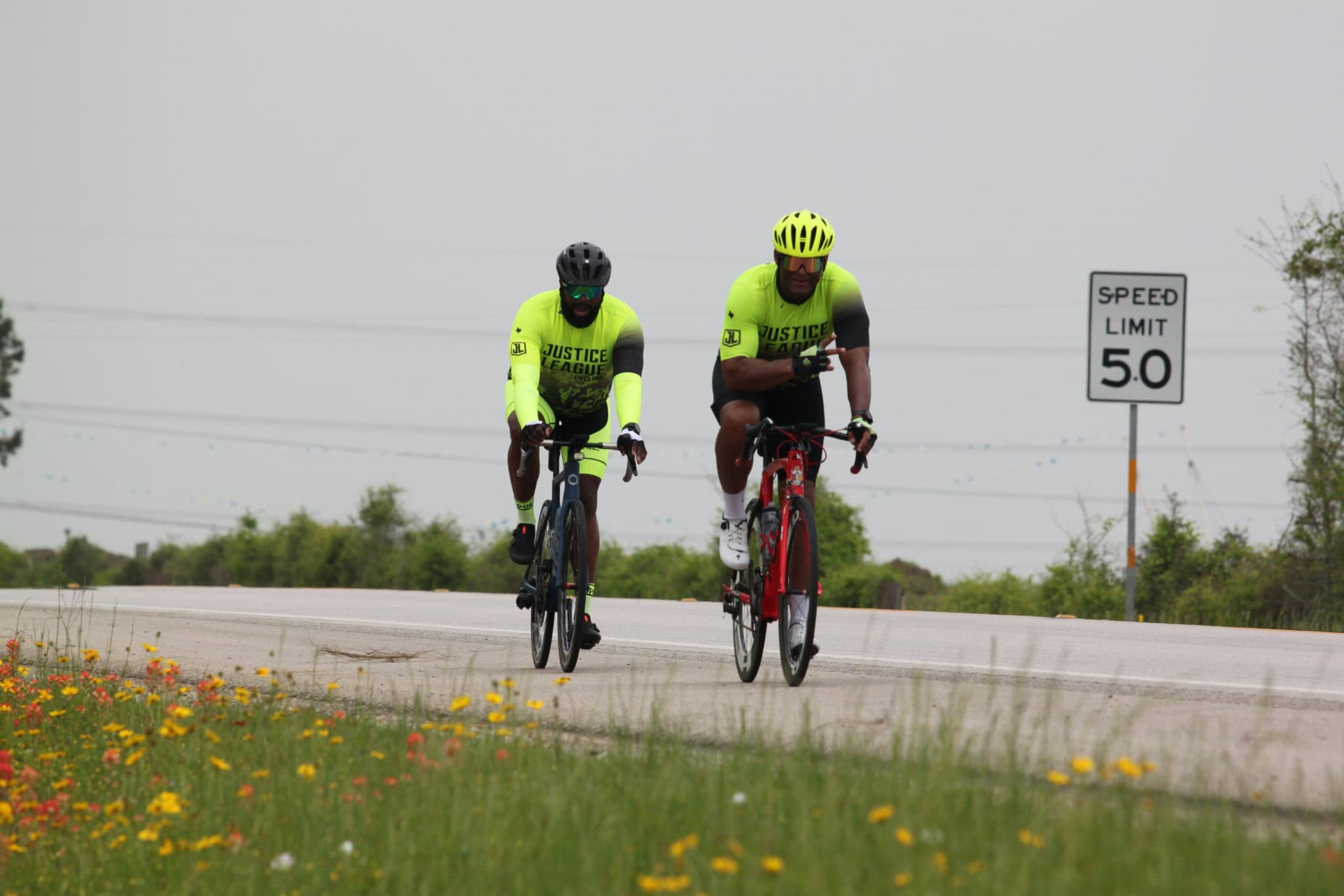 Bright neon cyclists from Justice League riding bikes on rural road during daytime.