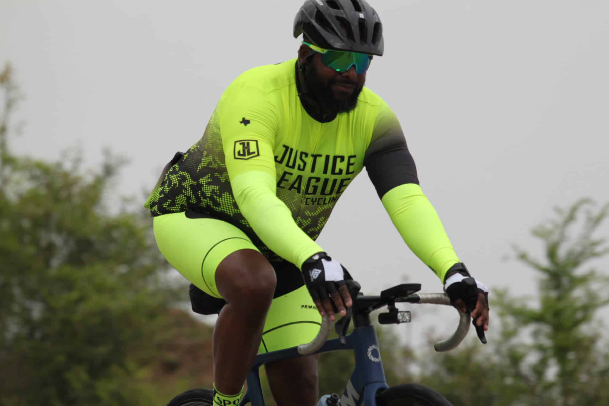 High-visibility cyclist wearing Justice League Cycling gear, riding on a scenic outdoor trail.