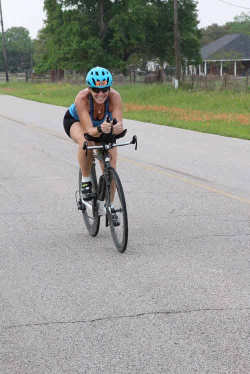 Bright female cyclist wearing a blue helmet riding a black road bike on a rural road during daytime.