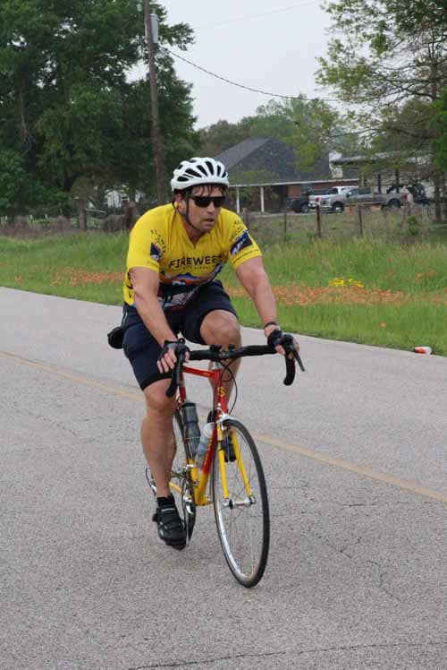 Rider wearing yellow jersey cycling on a suburban street during daytime.