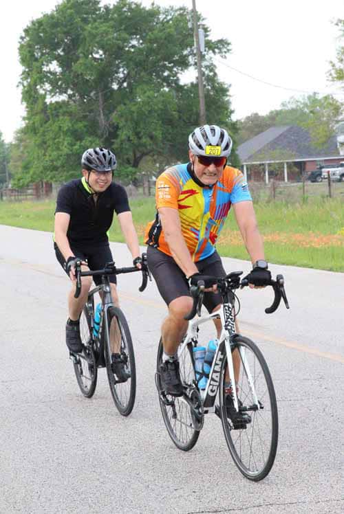 Brightly dressed cyclists riding along a rural road during daytime for Bluebonnet Express event.