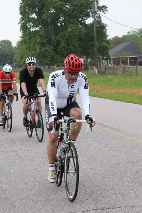A person riding a road bike during a cycling event outdoors with others in the background.