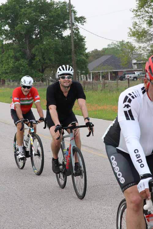 High school cyclists riding on a rural road, engaging in community cycling event.