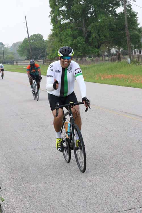- Cyclist riding on scenic rural road during Bluebonnet Express event with lush trees in background.