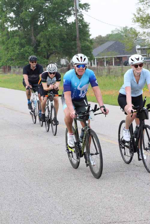 Bright cyclist group riding on rural road during daytime for Bluebonnet Express event.