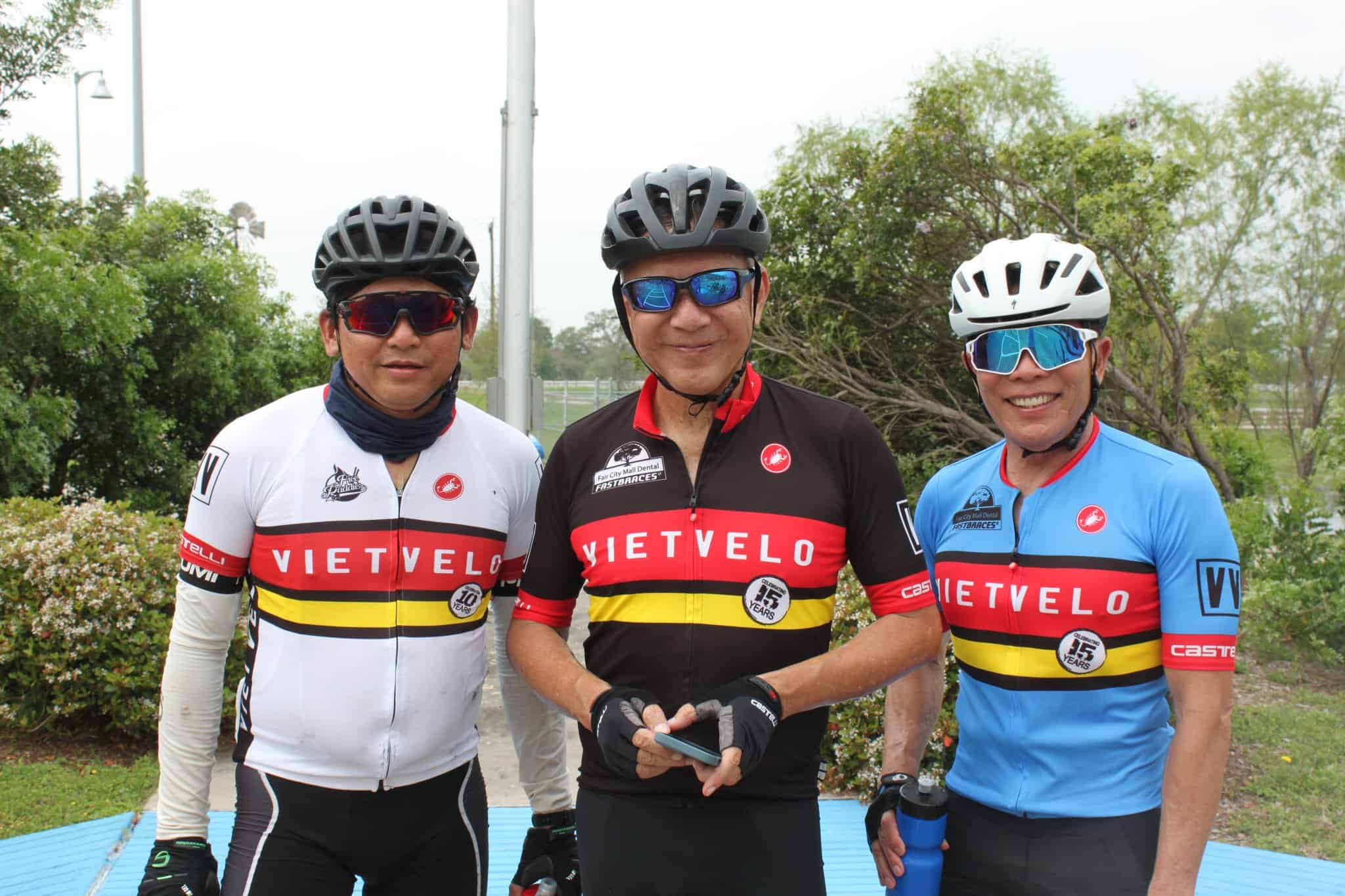 VietVelo cycling team members in colorful team jerseys outdoors with greenery, ready for a ride.