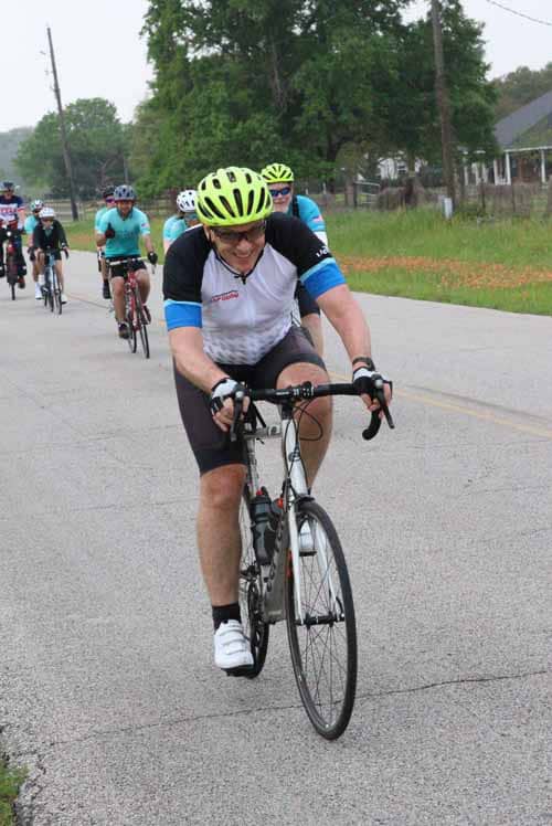 Bright yellow helmet, group of cyclists riding on rural road during Bluebonnet Express event.
