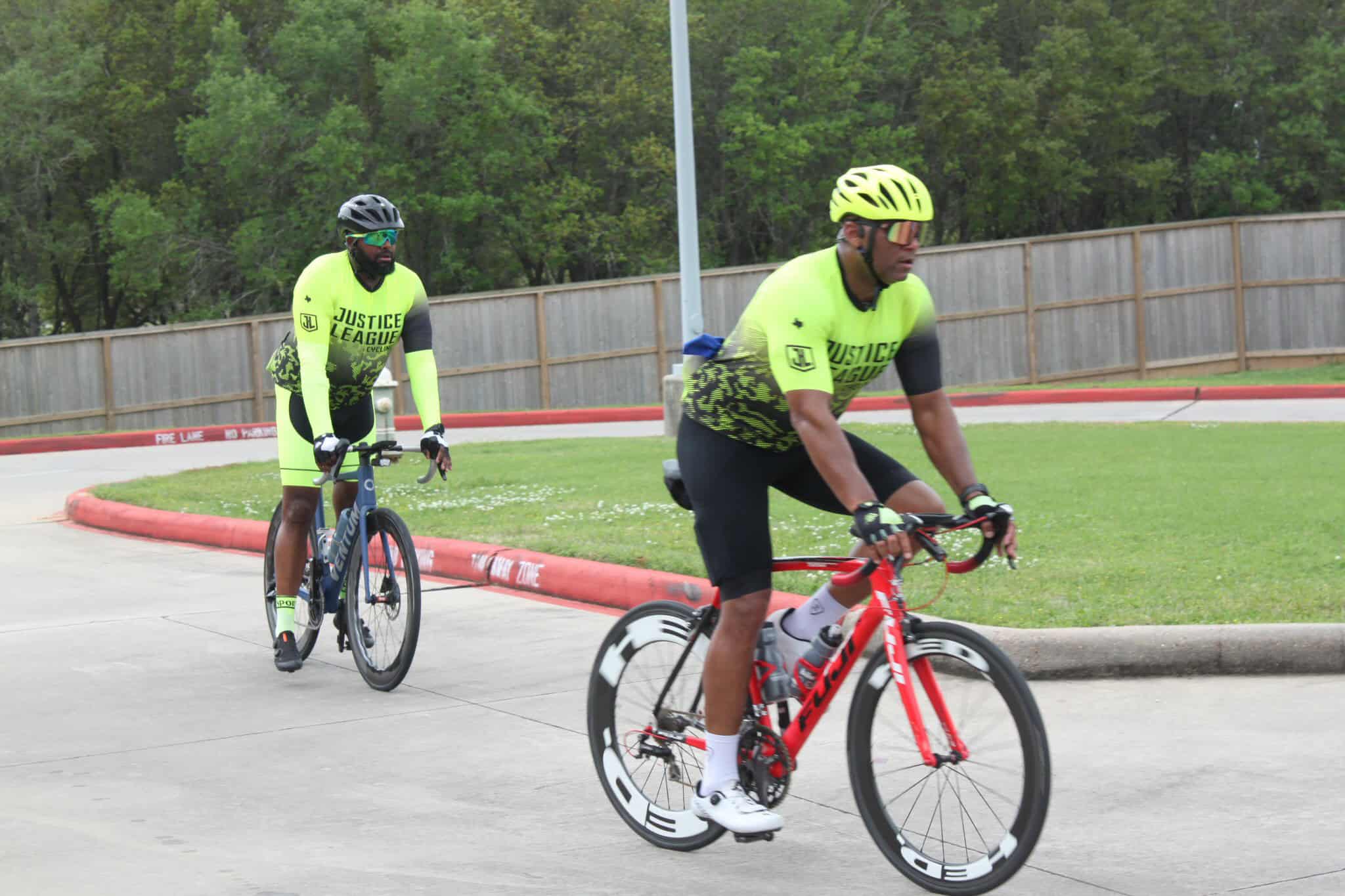 Cyclists wearing Justice League cycling jerseys on trail.