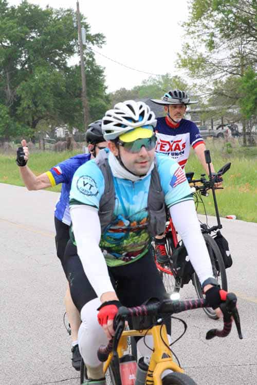 Velo cyclist in colorful jersey with companions riding on rural road during daytime.