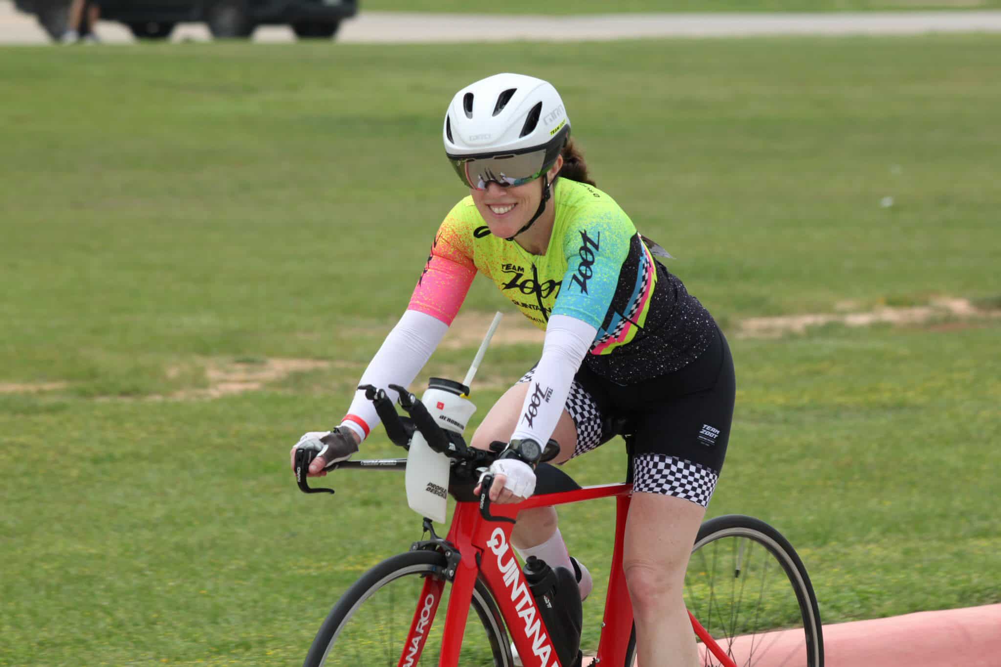 Bright female cyclist riding a red QWAVARRO bike during a race, wearing colorful gear, helmet, and sunglasses.