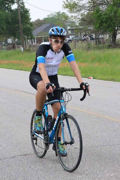 High-performance cyclist riding blue road bike on suburban street, promoting Bluebonnet Express cycling events.