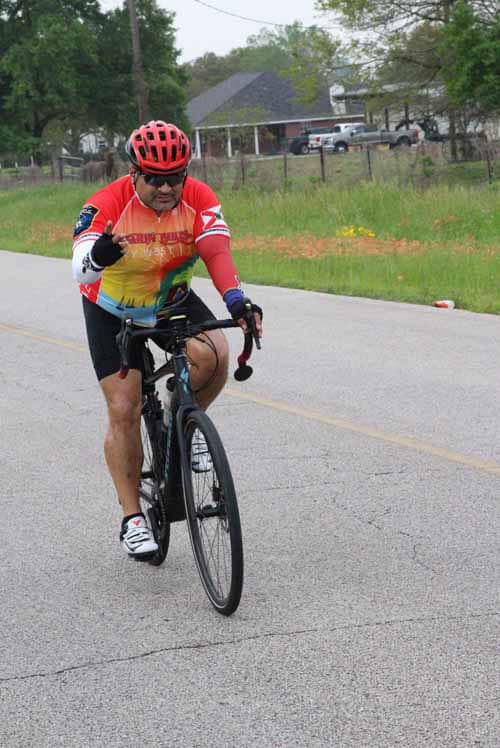 Brightly colored cyclist wearing a red helmet riding bike on rural road.