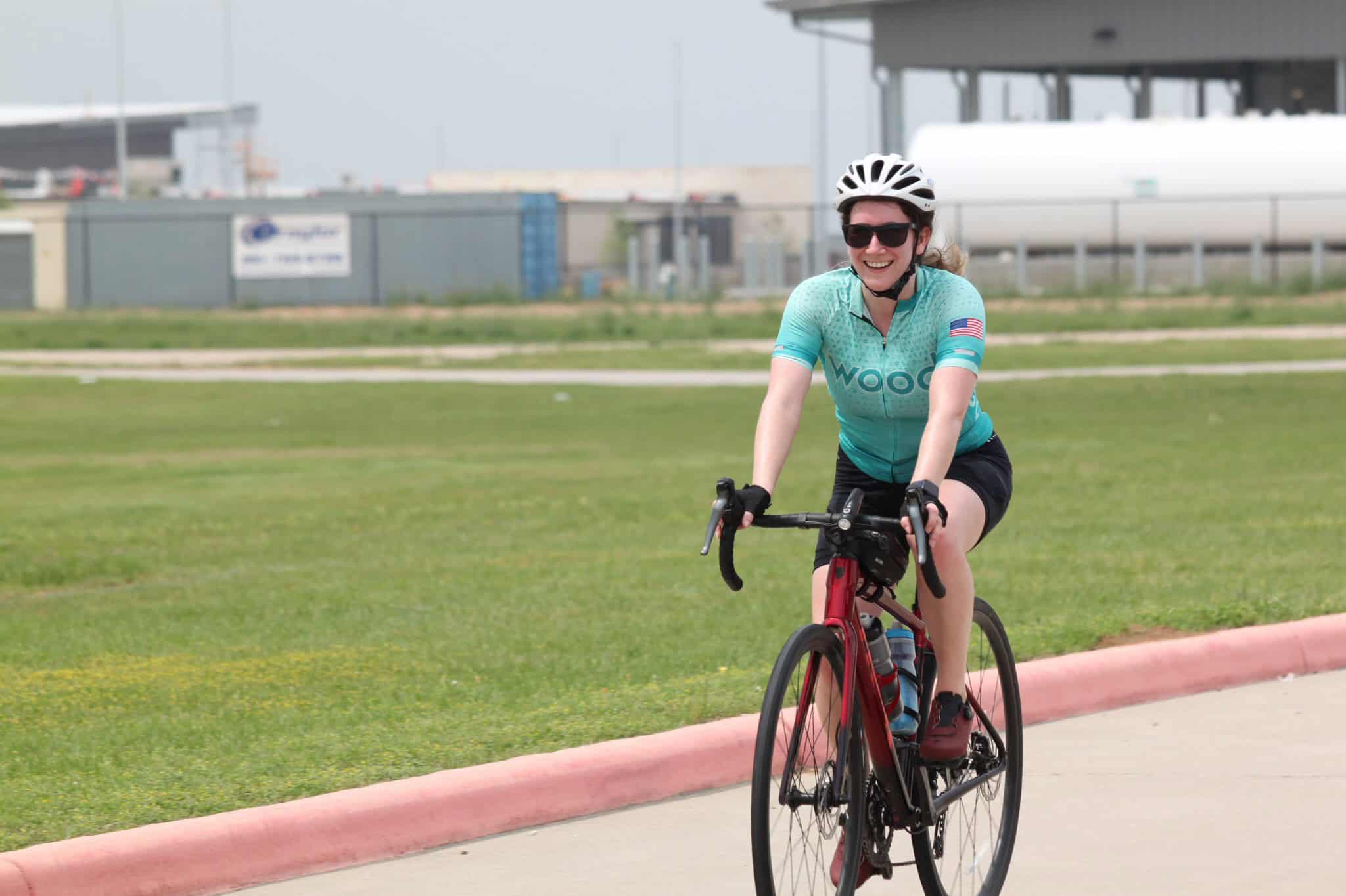 Bright woman cycling outdoors on a road bike wearing a helmet and sunglasses, enjoying a sunny day.