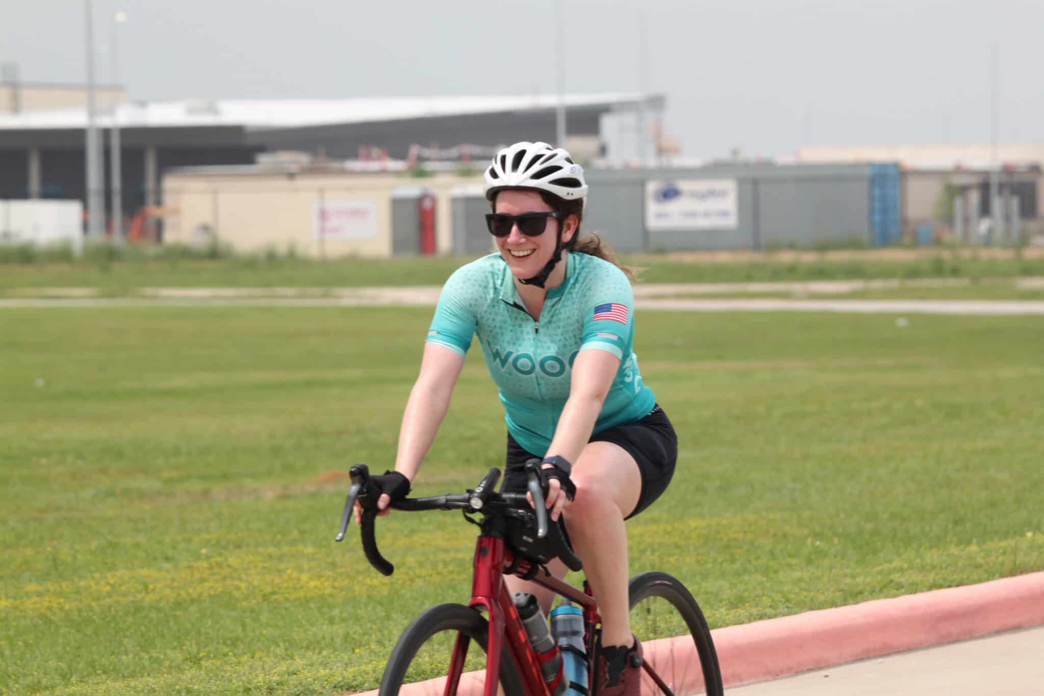 Bright woman riding a bicycle in Bluebonnet Express cycling event, smiling, wearing helmet and sunglasses.