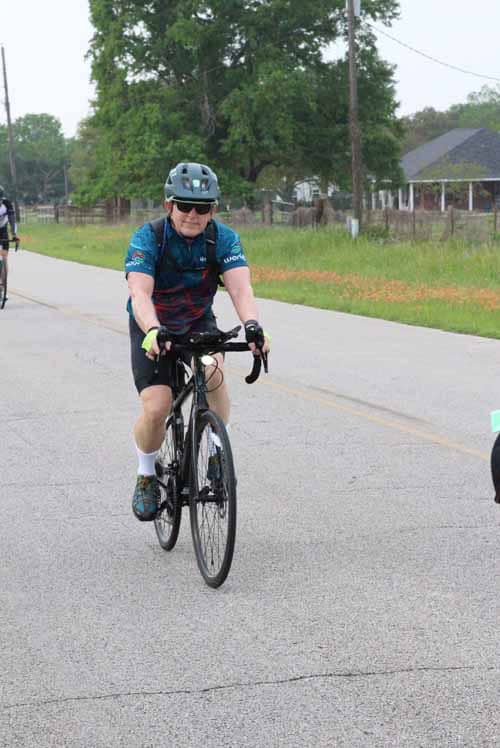 Bike rider with helmet and sunglasses cycling on rural road during Bluebonnet Express event.