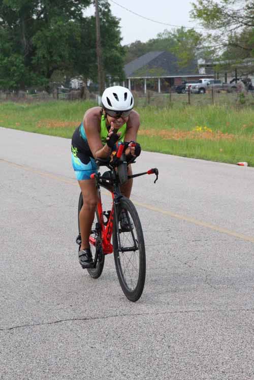 Bright-eyed cyclist in helmet making peace sign during Bluebonnet Express ride on scenic rural road.