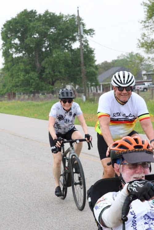 1. Smiling cyclists riding bikes on suburban road during daytime.