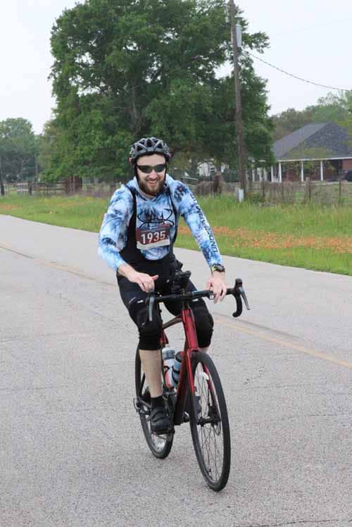 Bright-eyed cyclist wearing a helmet and sunglasses riding a bike during Bluebonnet Express event.