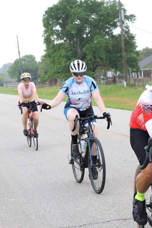 Bright female cyclist wearing a blue Methodist jersey on a scenic road during Bluebonnet Express event.