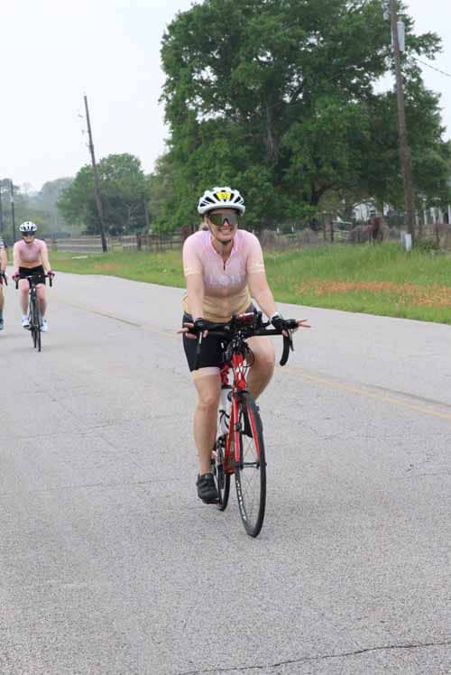 Bright woman cycling on rural road wearing helmet and sunglasses during daytime.