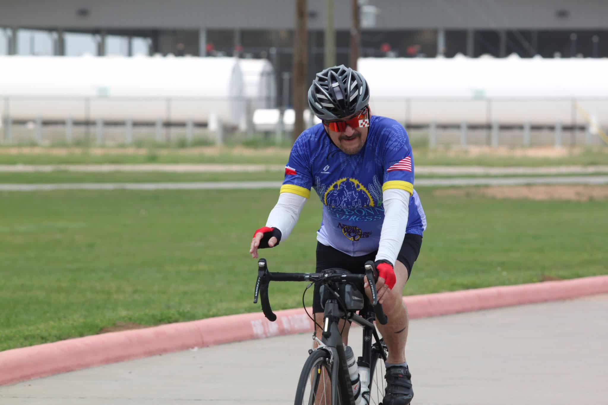 High-energy cyclist wearing Bluebonnet Express gear riding on city street during daytime.