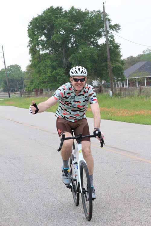 Man riding a bike on a sunny day, wearing a helmet and sunglasses, enjoying outdoor cycling.