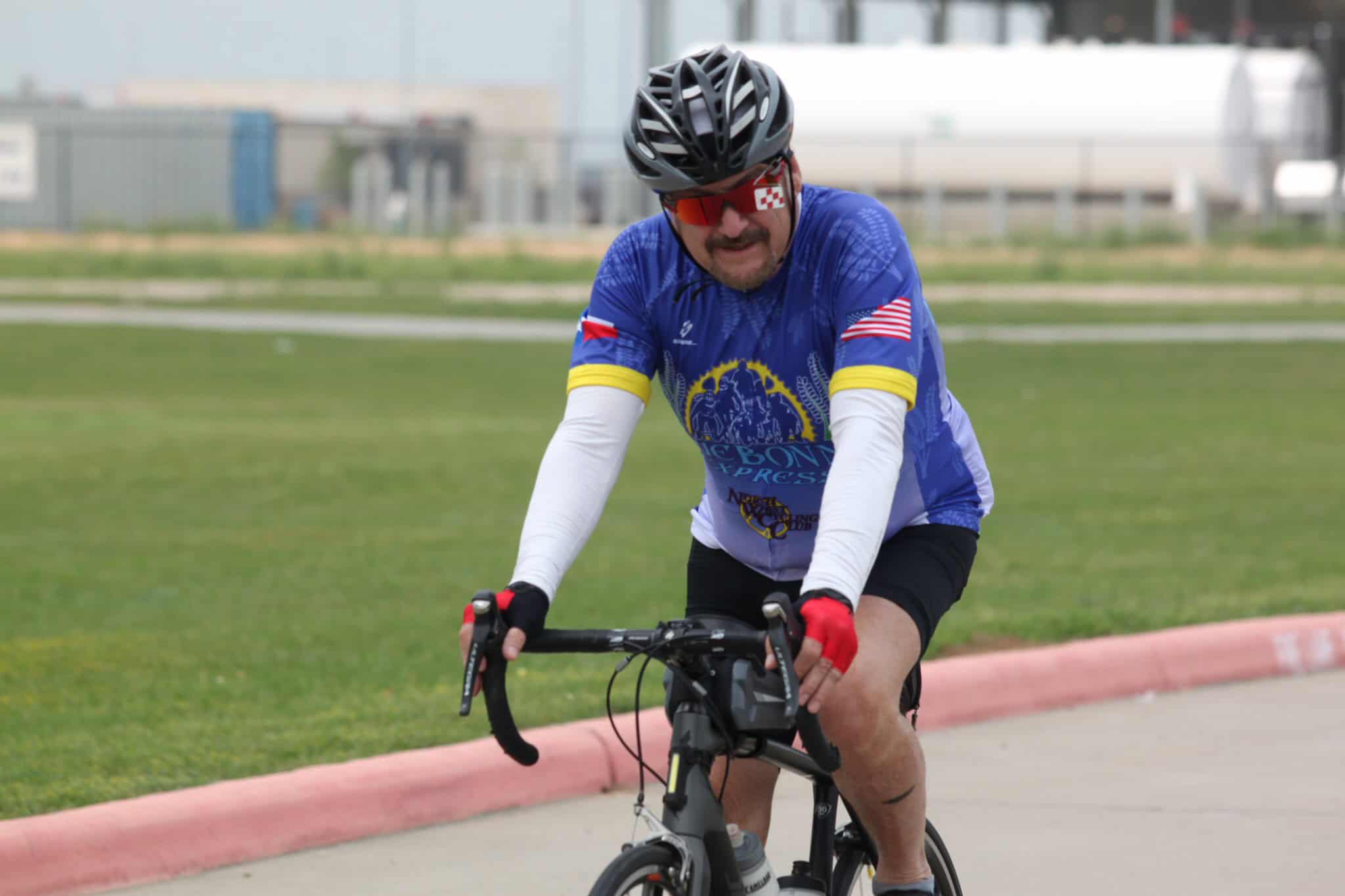 Bike rider in Bluebonnet Express cycling jersey riding on paved path.