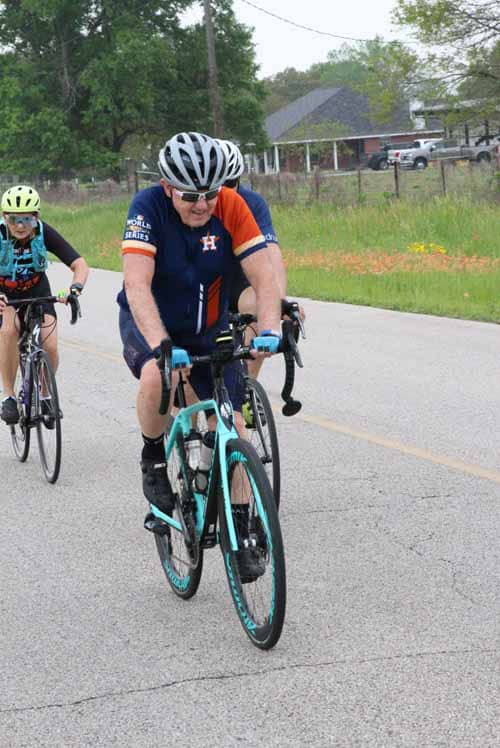 Bright cyclist wearing a Houston Astros jersey riding a road bike during Bluebonnet Express event.