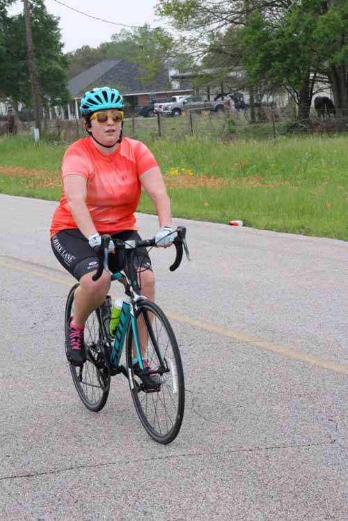 Bright woman biking in outdoor setting with green trees and rural background, emphasizing cycling and outdoor activity.