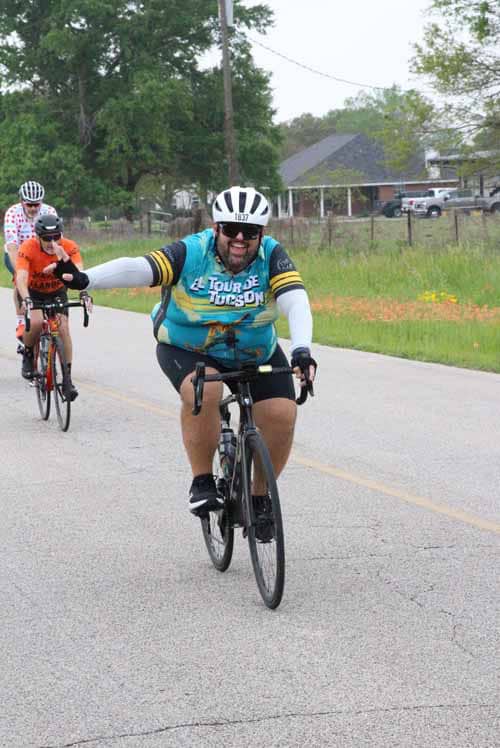 Smiling cyclist riding on rural road during Bluebonnet Express event for charity and adventure.