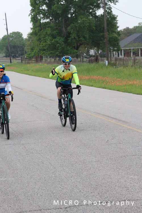 - Cyclist wearing bright yellow and blue riding on rural road during Bluebonnet Express event.