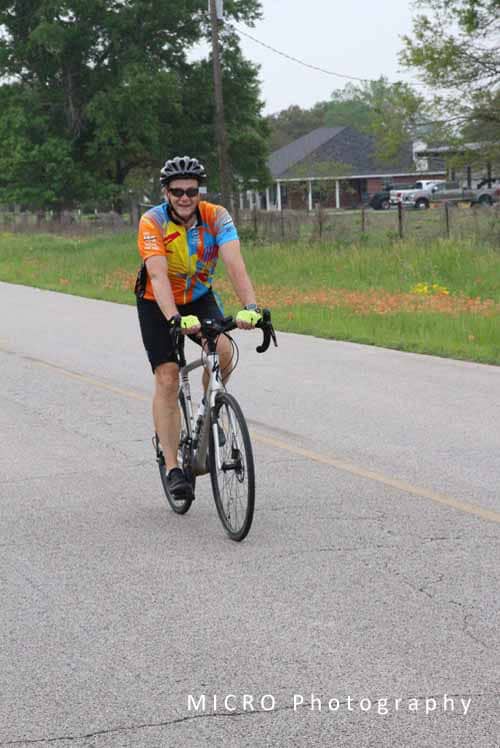 Bright cyclist riding on country road wearing colorful jersey and helmet for Bluebonnet Express event.
