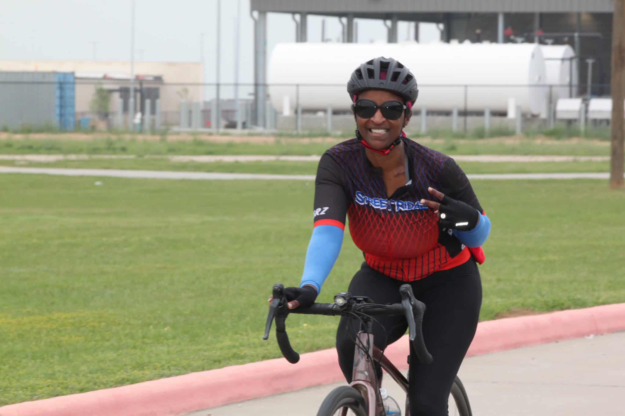 Bright smiling woman riding a bicycle on the street, wearing a helmet and cycling gear, promoting Bluebonnet Express bike services.