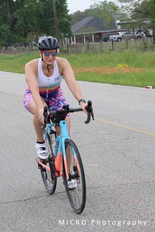 Bright female cyclist riding a bike on a suburban road during daytime for Bluebonnet Express event.