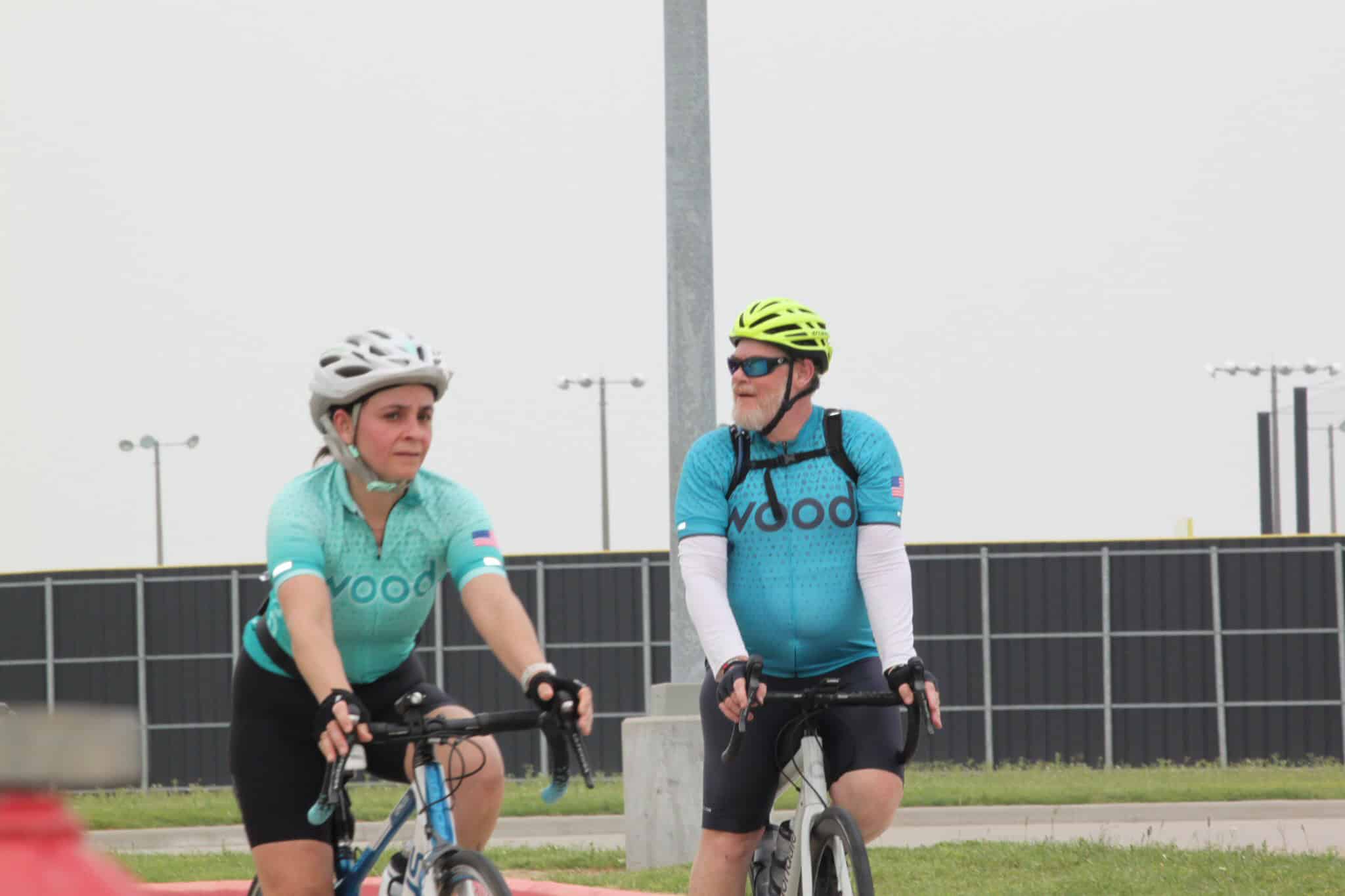 Bright blue cycling jerseys with "Voodoo" logo, two cyclists riding on paved trail, outdoor sports, health, fitness, bike ride.