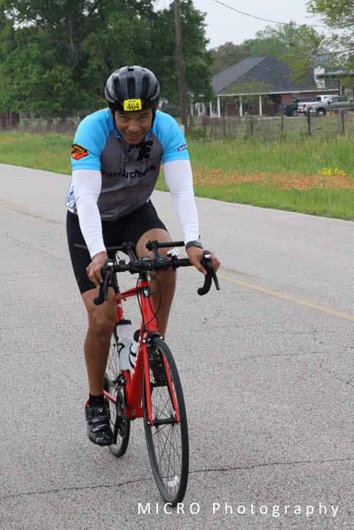 Bright blue and gray cycling jersey worn by cyclist riding on rural road during Bluebonnet Express event.