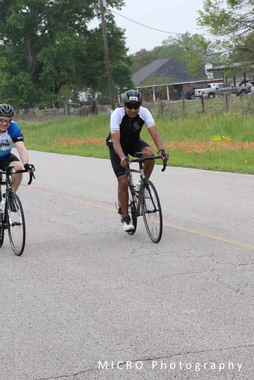 Bright blue bicycle helmet and cycling gear on a cyclist riding on a rural road during daytime.
