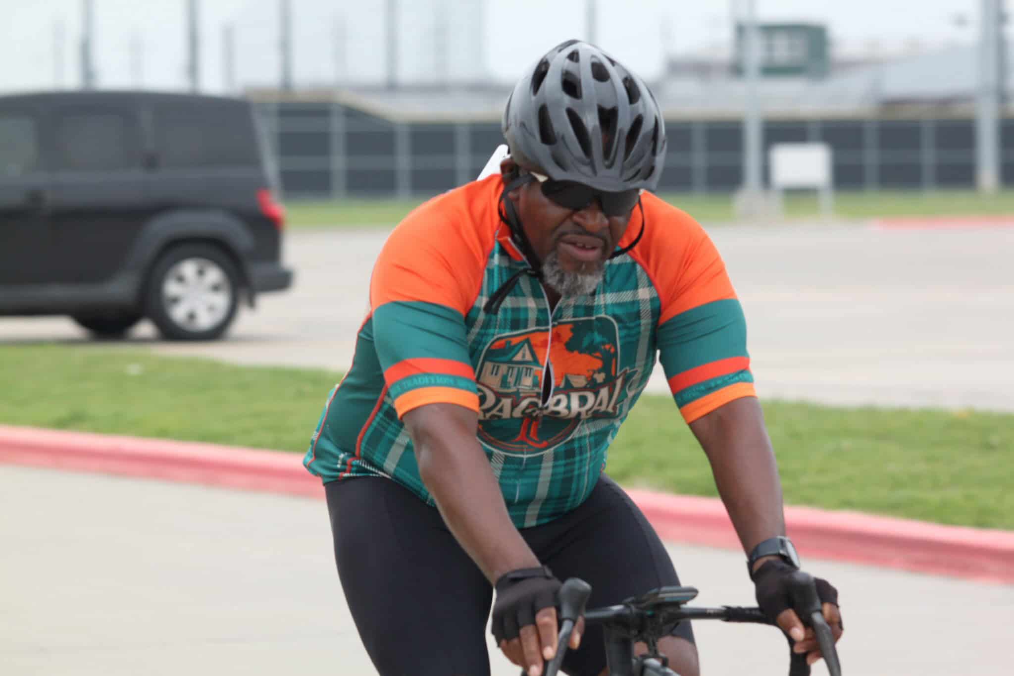 Vibrant man cycling outdoors wearing a colorful sports jersey and safety helmet, promoting Bluebonnet Express bike travel.