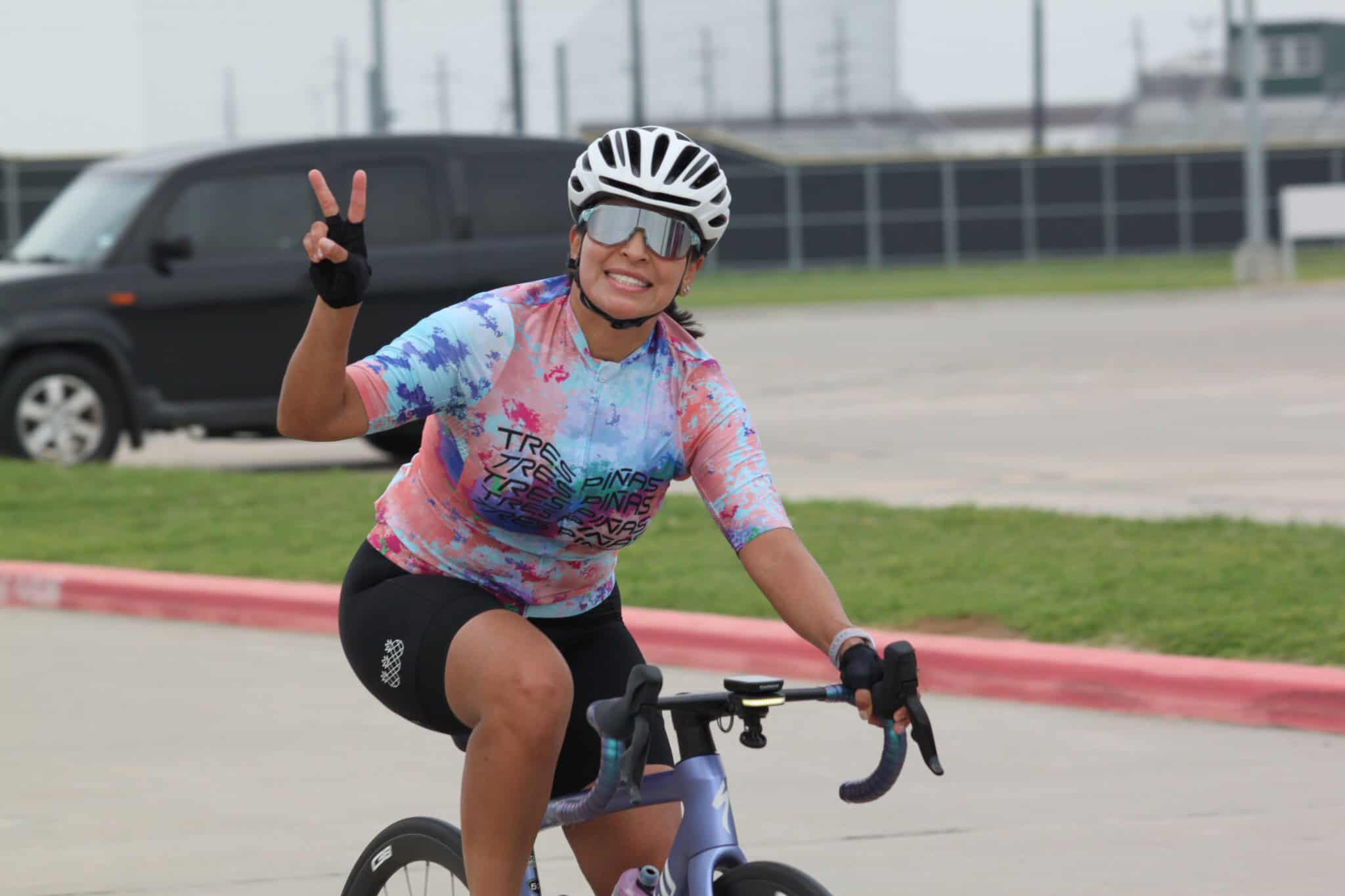 Cyclist wearing colorful jersey, making peace sign, on a scenic ride with Bluebonnet Express.
