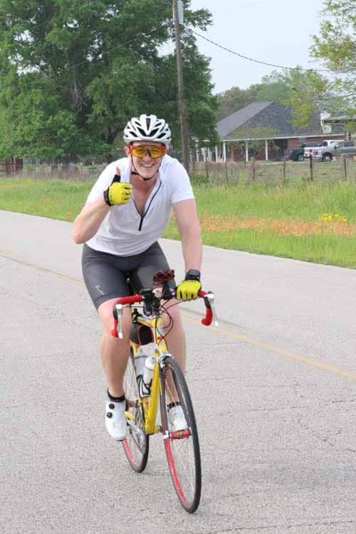 Bright female cyclist enjoying outdoor ride on a road bike, wearing helmet and sunglasses for safety.