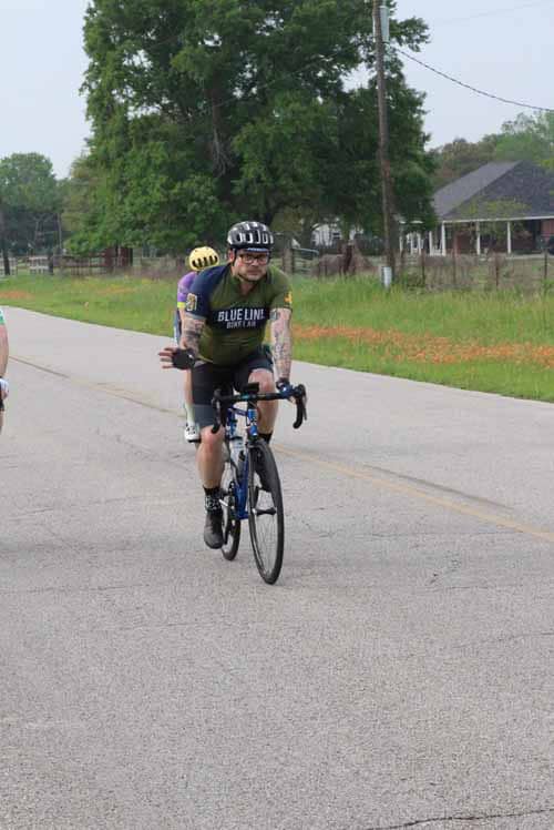 Cyclist riding on the road with Bluebonnet Express cycling team gear in Texas countryside.
