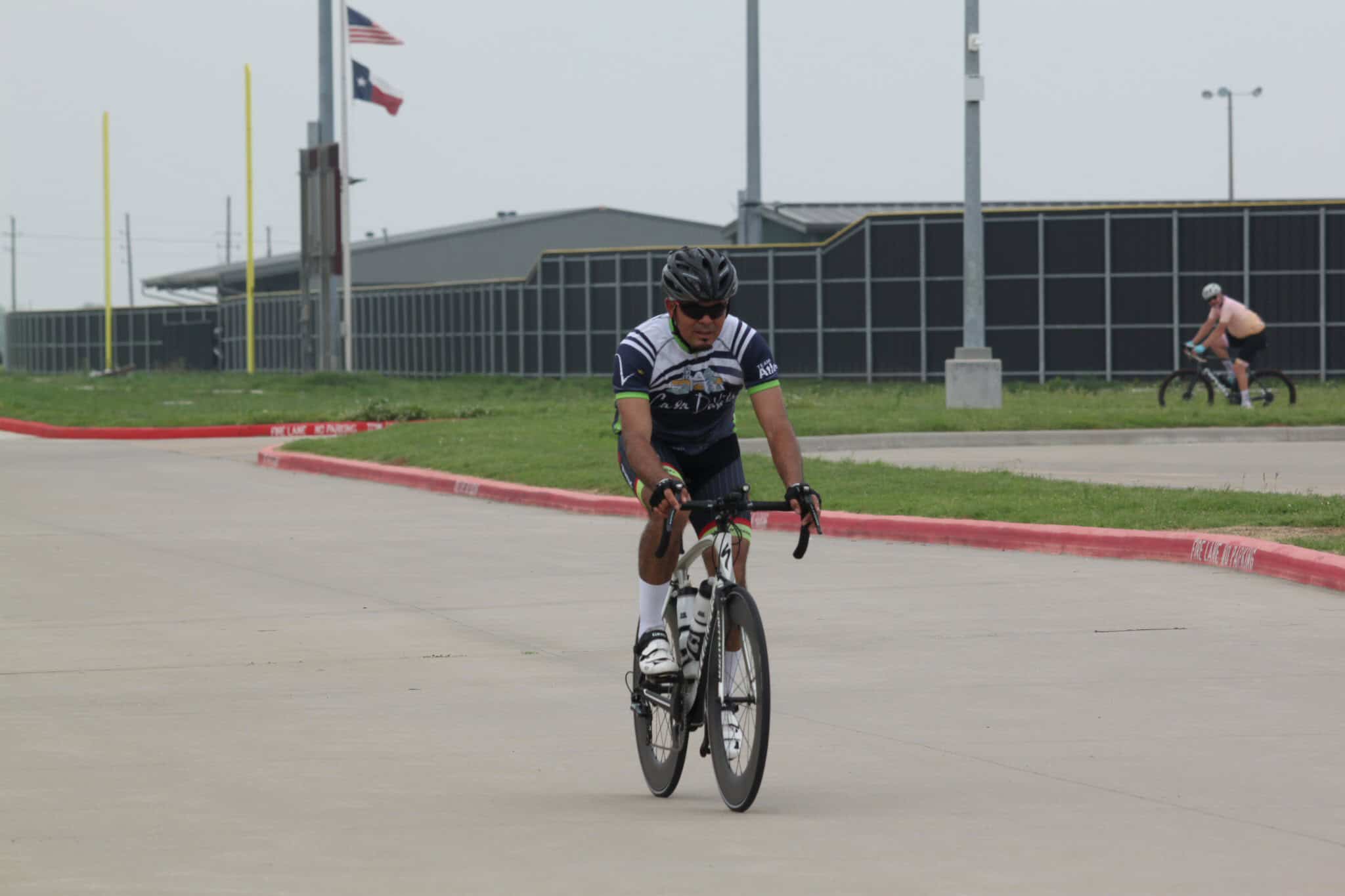 Road cyclist riding on a paved street with Texas flags in the background.